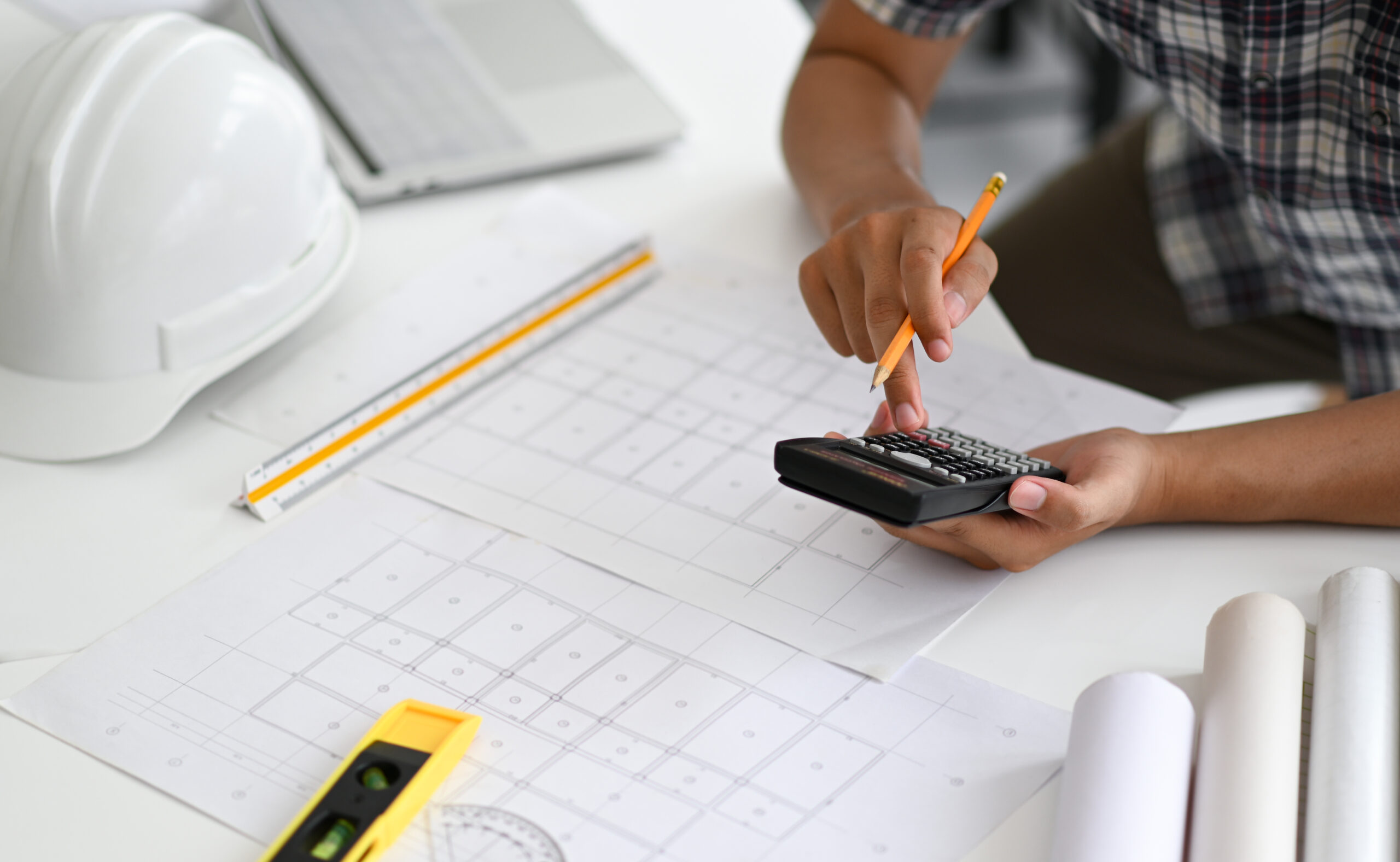 Architects are using a calculator to estimate the cost of house plans, house plans, safety helmet and office equipment placed on the desk.